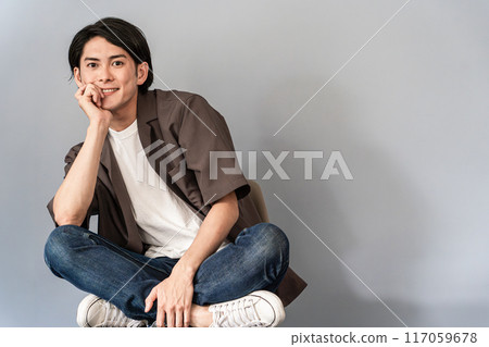 一個穿著運動鞋和牛仔褲的清爽男人坐在椅子上 一個穿著運動鞋和牛仔褲的清爽男人坐在椅子上 117059678