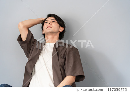 一個年輕的亞洲男子坐在椅子上思考（擔心、沮喪、負面、未來、遺憾、換工作、就業、教育背景） 117059753