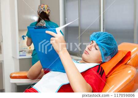 Young male patient reading  an informed consent just before getting a small surgery procedure at the dermatologist office. 117059806