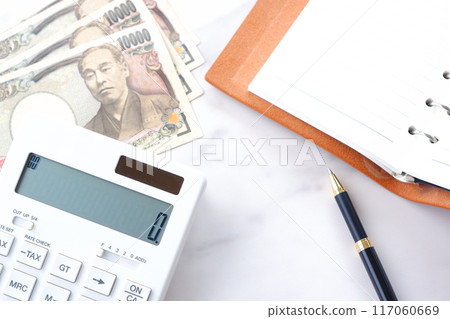 桌上放著環形筆記本、計算機和一張印有福澤諭肖像的一萬日圓鈔票。 桌上放著環形筆記本、計算機和一張印有福澤諭肖像的一萬日圓鈔票。 117060669