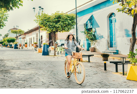 Beautiful and happy girl riding a bicycle on the street of La Calzada, Granada, Nicaragua. Tourist woman riding a bicycle on the streets of Granada 117062237
