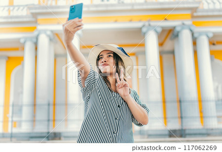 Beautiful tourist girl taking selfie in the cathedral of Granada. Young tourist woman with hat taking selfie in a square. Selfies and vacation concept Beautiful tourist girl taking selfie in the cathedral of Granada. Young tourist woman with hat taking selfie in a square. Selfies and vacation concept 117062269