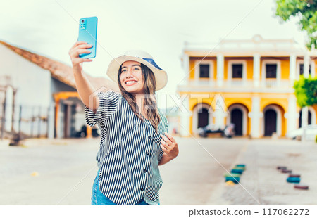 Happy tourist girl taking selfie in the cathedral of Granada. Young travel woman with hat taking a selfie in a square Happy tourist girl taking selfie in the cathedral of Granada. Young travel woman with hat taking a selfie in a square 117062272