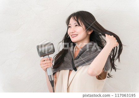 A woman blow-drying her hair with a hair dryer (hair care) A woman blow-drying her hair with a hair dryer (hair care) 117063195