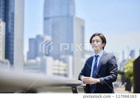 A Japanese businessman checks his watch against the backdrop of skyscrapers. A Japanese businessman checks his watch against the backdrop of skyscrapers. 117066163