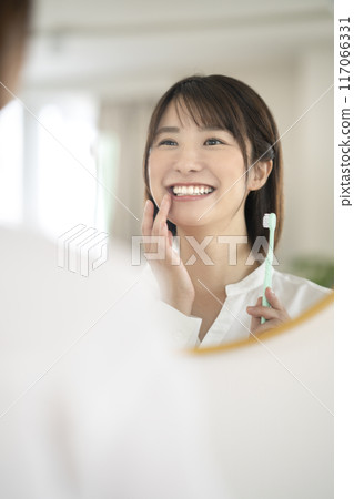 A woman in her 30s brushing her teeth while looking in the mirror A woman in her 30s brushing her teeth while looking in the mirror 117066331