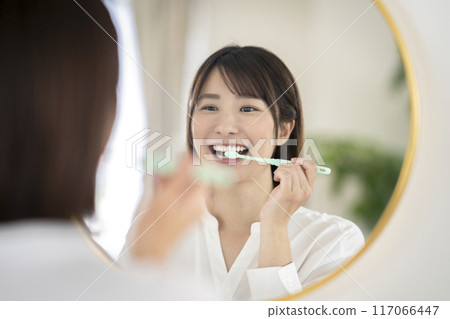 Young woman brushing her teeth while looking in the mirror 117066447