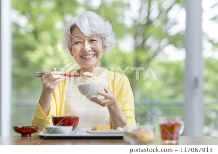 Senior woman eating, looking at camera, smiling Senior woman eating, looking at camera, smiling 117067913