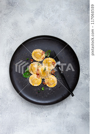 fresh ravioli, with butter, spices and herbs, fried bacon, on a black plate, top view, dark background, no people, 117068589