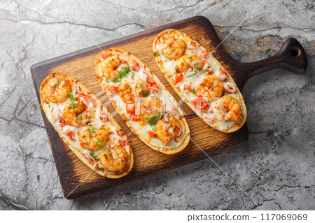 Open baked panini sandwiches with shrimps, cheese, garlic and tomatoes close-up on a wooden board. Horizontal top view 117069069