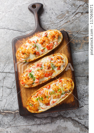Baked Cheesy Shrimp Garlic Bread with mozzarella, tomatoes and parsley closeup on the wooden board. Vertical top view Baked Cheesy Shrimp Garlic Bread with mozzarella, tomatoes and parsley closeup on the wooden board. Vertical top view 117069071