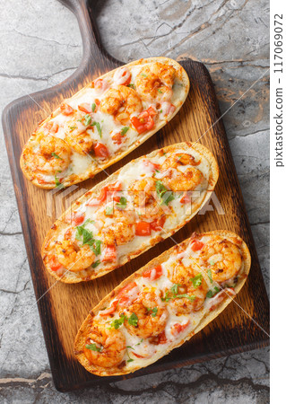 Hot baked sandwiches with shrimps, cheese, garlic and tomatoes close-up on a wooden board. Vertical top view 117069072