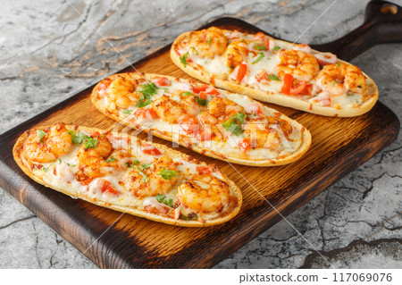 Open baked panini sandwiches with shrimps, cheese, garlic and tomatoes close-up on a wooden board. Horizontal Open baked panini sandwiches with shrimps, cheese, garlic and tomatoes close-up on a wooden board. Horizontal 117069076
