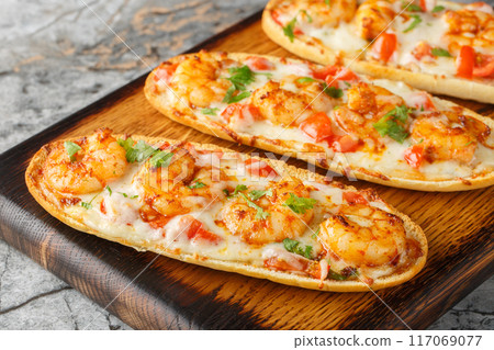 Mozzarella shrimps open sandwiches baked on Italian garlic bread close-up on a wooden board. Horizontal 117069077