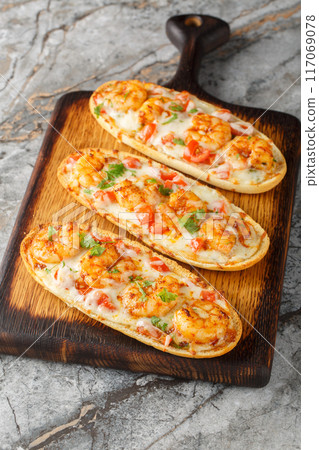 Baked Cheesy Shrimp Garlic Bread with mozzarella, tomatoes and parsley closeup on the wooden board. Vertical 117069078