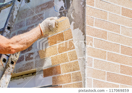 House painter sticks brick wall panel on House facade. House painter sticks brick wall panel on House facade. 117069859