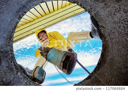 Man immerses waste pump into wastewater through hole in concrete well ring, seen from below. Man immerses waste pump into wastewater through hole in concrete well ring, seen from below. 117069884