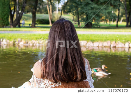 A woman is sitting in front of a lake filled with ducks A woman is sitting in front of a lake filled with ducks 117070170