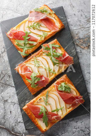 Appetizer pear jamon puff pastry pies for buffet and parties close-up on marble board. Vertical top view 117072612