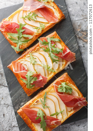 Puff pastry sandwich with pear, ham and arugula close-up on marble board. Vertical top view Puff pastry sandwich with pear, ham and arugula close-up on marble board. Vertical top view 117072613