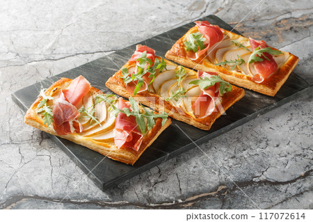Savory Puff pastry pies with pear, jamon and arugula close-up on a marble board. Horizontal Savory Puff pastry pies with pear, jamon and arugula close-up on a marble board. Horizontal 117072614