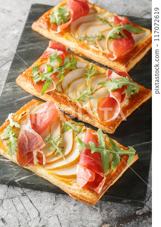 Appetizer pear jamon puff pastry pies for buffet and parties close-up on marble board. Vertical Appetizer pear jamon puff pastry pies for buffet and parties close-up on marble board. Vertical 117072619