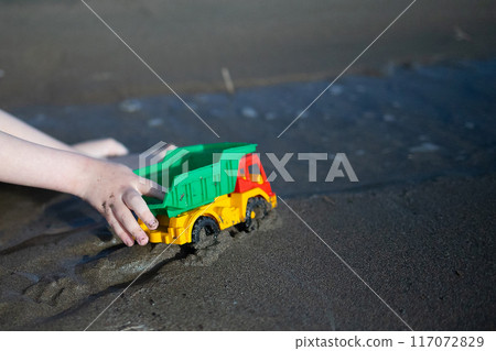 A child plays with a toy dump truck in the sand at the beach A child plays with a toy dump truck in the sand at the beach 117072829