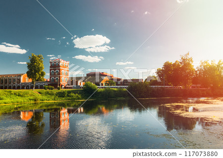 Peaceful and picturesque reflection of a serene river showcasing scenic buildings and lush greenery 117073880