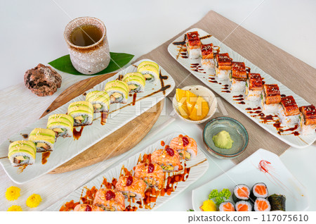Ceramic tray with variety of salmon sushi roll with vegetables, avocado roll, grilled eel unagi in japanese restaurant Ceramic tray with variety of salmon sushi roll with vegetables, avocado roll, grilled eel unagi in japanese restaurant 117075610