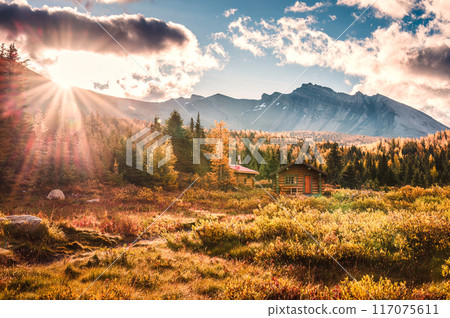 Sunrise shining over wooden huts with rocky mountains in autumn forest at Assiniboine provincial park, Canada 117075611