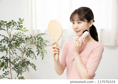 一位女士一邊照鏡子一邊使用臉部美容儀 117076329