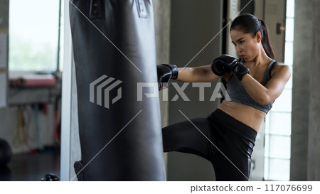 Asian boxing athlete woman kick big punching bag at fitness gym Asian boxing athlete woman kick big punching bag at fitness gym 117076699