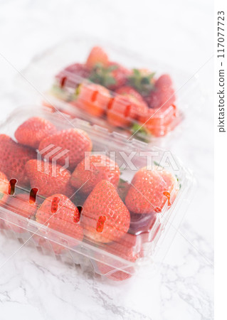 Fresh strawberries are showcased in their original store-bought plastic container, resting on a kitchen counter, ready to be washed, eaten, or stored. Fresh strawberries are showcased in their original store-bought plastic container, resting on a kitchen counter, ready to be washed, eaten, or stored. 117077723