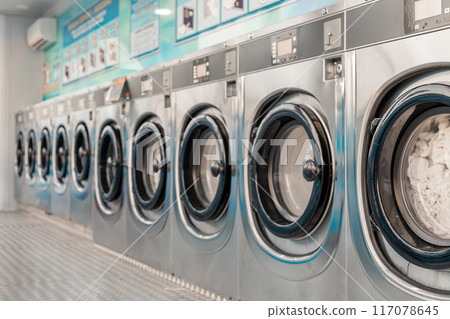 Row of washing machines in public laundry. Commercial cleaning services or utility management in communal spaces. Laundromat. Shared amenities. Self-service, coin laundry, or coin wash. Row of washing machines in public laundry. Commercial cleaning services or utility management in communal spaces. Laundromat. Shared amenities. Self-service, coin laundry, or coin wash. 117078645