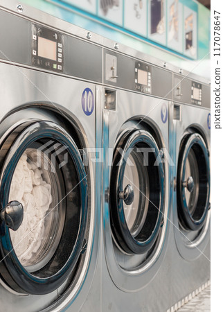 Row of washing machines in public laundry. Commercial cleaning services or utility management in communal spaces. Laundromat. Shared amenities. Self-service, coin laundry, coin wash. Vertical picture. Row of washing machines in public laundry. Commercial cleaning services or utility management in communal spaces. Laundromat. Shared amenities. Self-service, coin laundry, coin wash. Vertical picture. 117078647