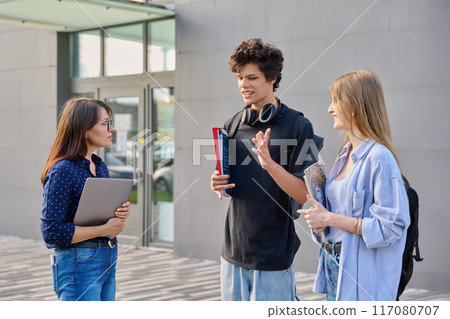 Group of college students talking with female teacher, educational building background 117080707