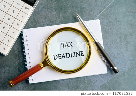 TAX DEADLINE words written through the lens of a magnifying glass in a notebook on a gray background 117081582