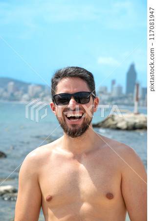 Young Hispanic man model smiling with sunglasses on beach looking to camera 117081947