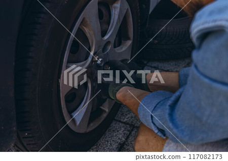 Young man in unscrewing lug nuts on car wheel in process of new tire replacement,using wrench while changing flat tire on the road. 117082173