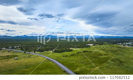 Aerial Fly Over Lush Green Field and Mountain Range with Winding Rural Road 117082512