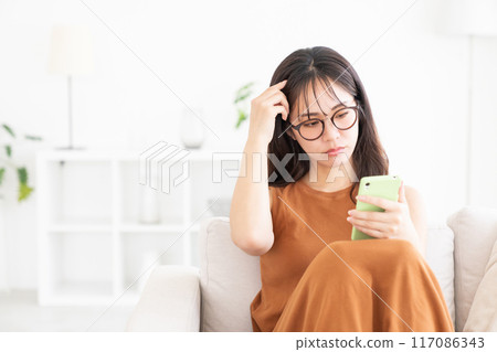 年輕女子在房間裡看智慧型手機 麻煩 年輕女子在房間裡看智慧型手機 麻煩 117086343