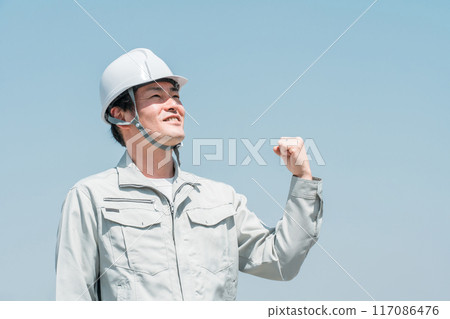 一名身穿工作服的亞洲男工戴著頭盔，仰望藍天下的天空 117086476