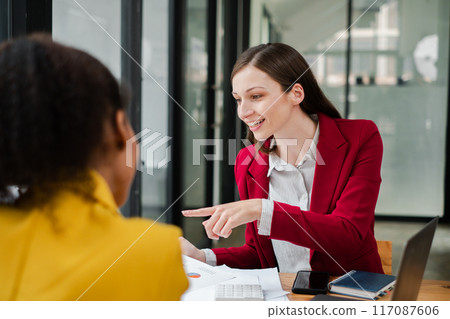 Two women engaged in a professional business meeting in a modern office, discussing documents and ideas. Two women engaged in a professional business meeting in a modern office, discussing documents and ideas. 117087606