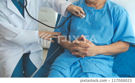 Doctor using stethoscope to listen senior man heart during examination in hospital room and wearing visor as safety precaution against coronavirus. Medical control for infections, disease. 117088023