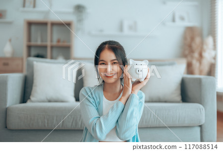 Young Asian woman holding piggy bank and sitting on the floor at home 117088514