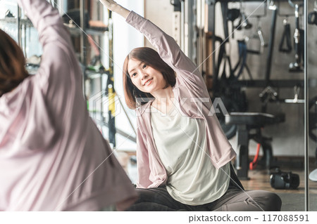 Young Asian woman doing stretching, warm-up and flexibility exercises in the stretching area of the gym 117088591