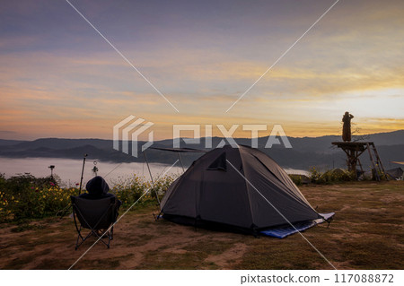 Tourist tent on camping site on the meadow next to the foggy during sunset, Thailand. Beautiful sunset twilight sky 117088872