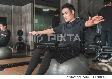 A man riding a balance ball in a gym 117089639
