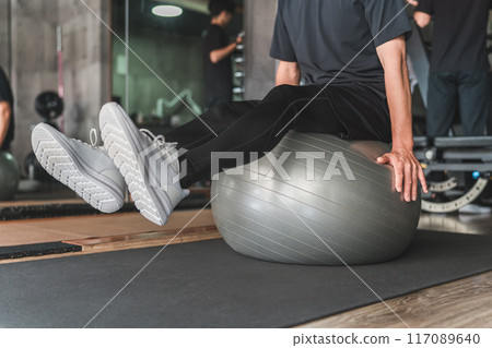 A man riding a balance ball in a gym A man riding a balance ball in a gym 117089640