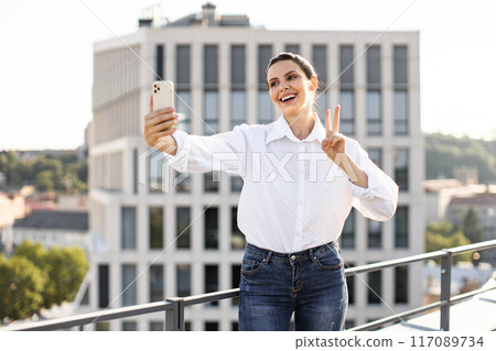 Woman taking selfie on rooftop making peace sign Woman taking selfie on rooftop making peace sign 117089734